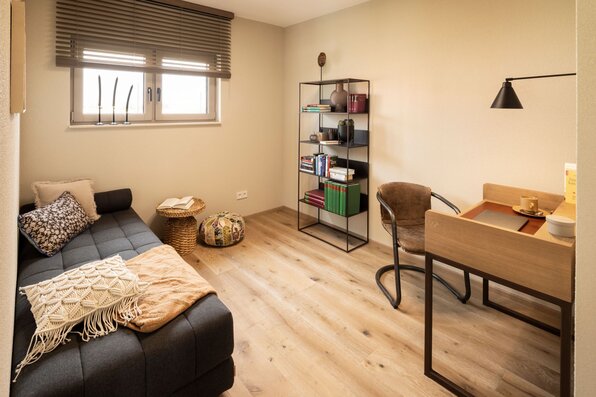 Arbeitszimmer im FingerHaus ARTIS 400 Musterhaus Schwarzwald mit Schreibtisch, Regal, gemütlichem Sofa und moderner Einrichtung in warmen Farben.