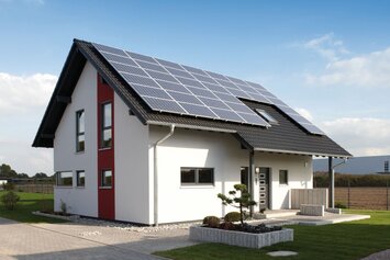 Modernes Einfamilienhaus mit rotem Fassadenelement und großer Photovoltaikanlage auf dem Dach – Musterhaus VIO 400 in Köln.