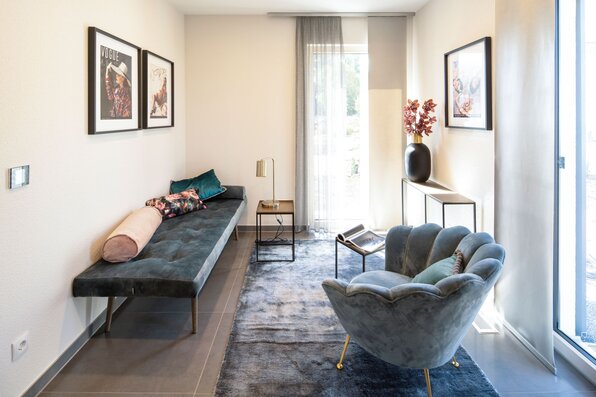 Elegantes Gästezimmer im Musterhaus MEDLEY 300 B in Frankenberg mit modernem Sessel, Sofa und stilvoller Wanddekoration.