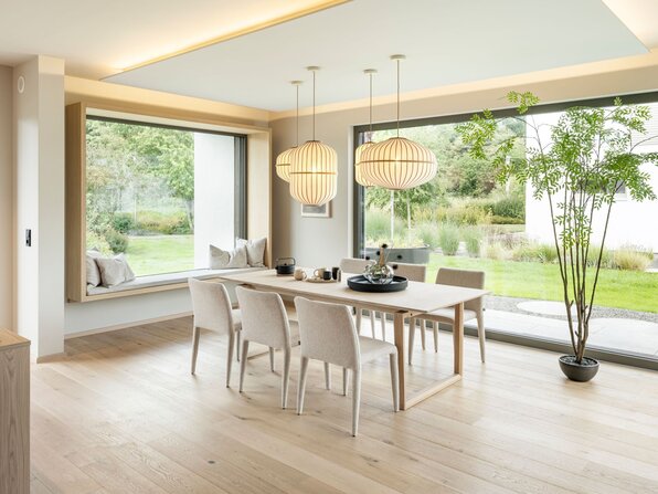 Essbereich im FingerHaus Musterhaus NIVO in Frankenberg mit Holztisch, sechs Stühlen, Pendelleuchten und großen Fensterflächen zum Garten.