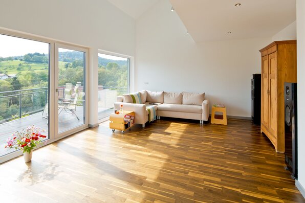 Helles Wohnzimmer in einem frei geplanten Finger-Haus mit großer Fensterfront, Zugang zum Balkon, heller Sofaecke und Holzfußboden.