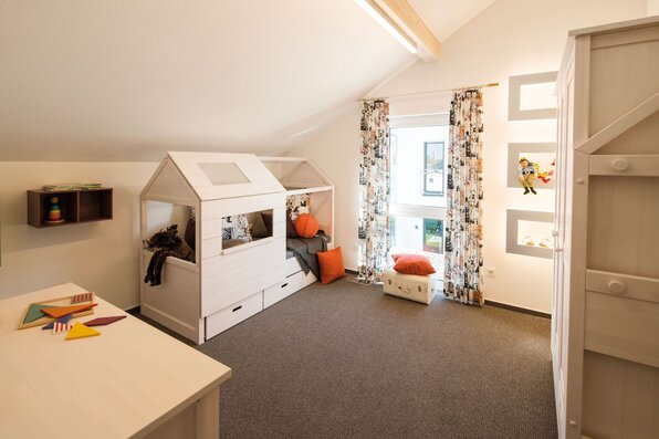 Kinderzimmer im FingerHaus NEO Musterhaus Günzburg mit kreativem Spielbett in Hausform, farbenfroher Dekoration und gemütlicher Atmosphäre.