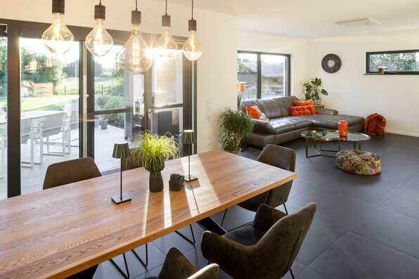 Helles Wohn- und Esszimmer in einem modernen FingerHaus mit großem Holztisch, stilvollen Hängelampen und gemütlicher Sitzecke.