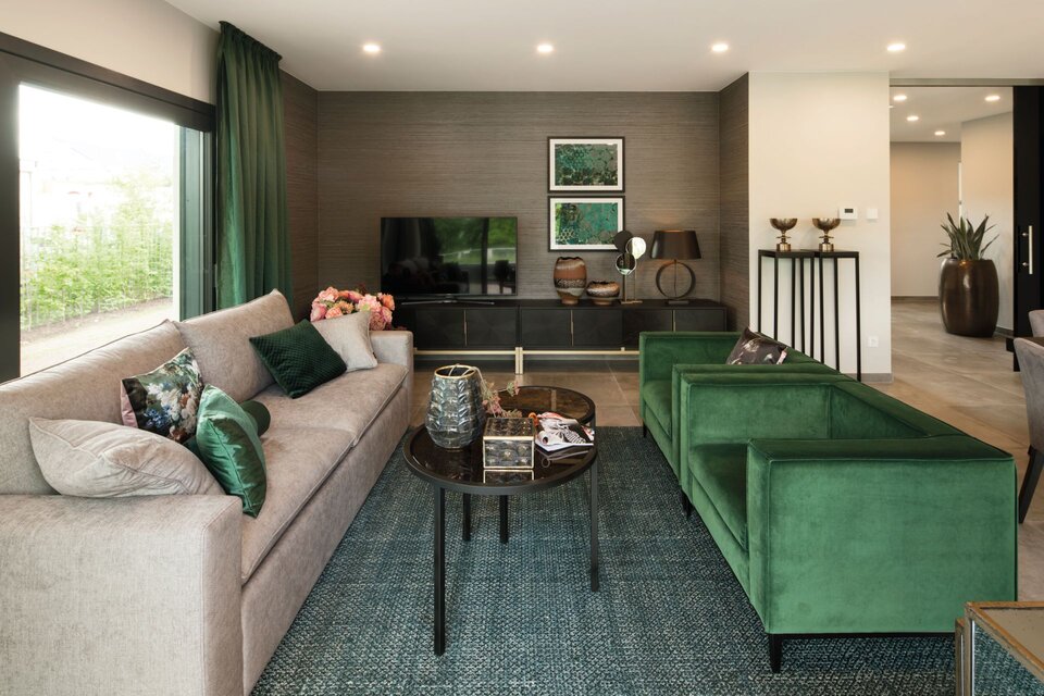 Modernes Wohnzimmer im Musterhaus ALTERO in Gießen mit stilvollem Sofa, grünen Designersesseln und eleganter Einrichtung.