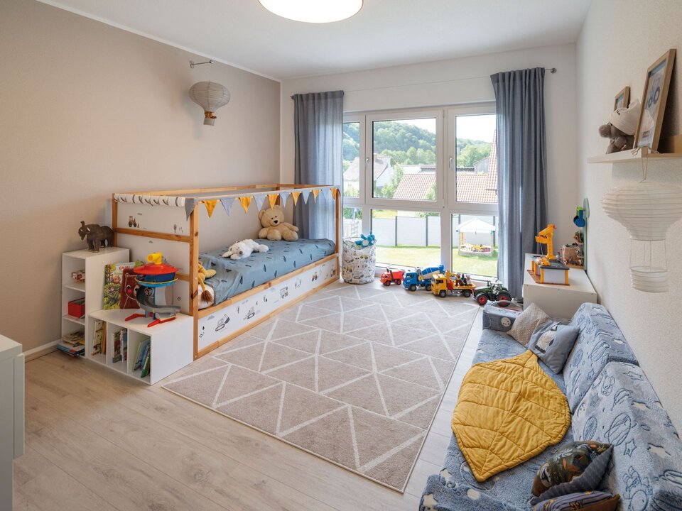 Kinderzimmer mit Hausbett, Spielzeugregalen und großem Teppich. Helles Fenster mit Vorhängen und freundliche Wandfarben schaffen eine spielerische Atmosphäre.