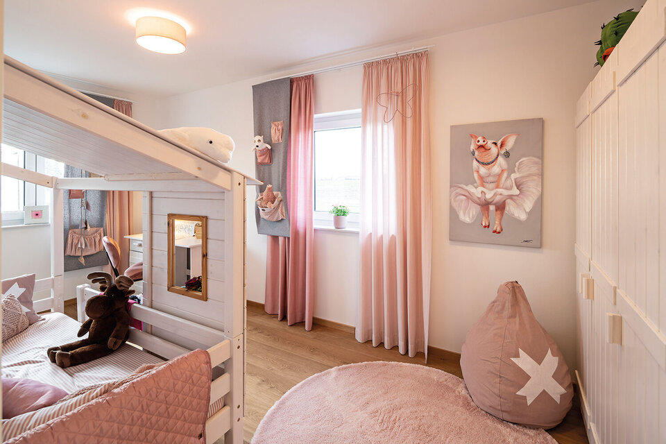 Kinderzimmer mit Etagenbett aus Holz, rosa Vorhängen, Sitzkissen und kindlicher Wanddekoration.