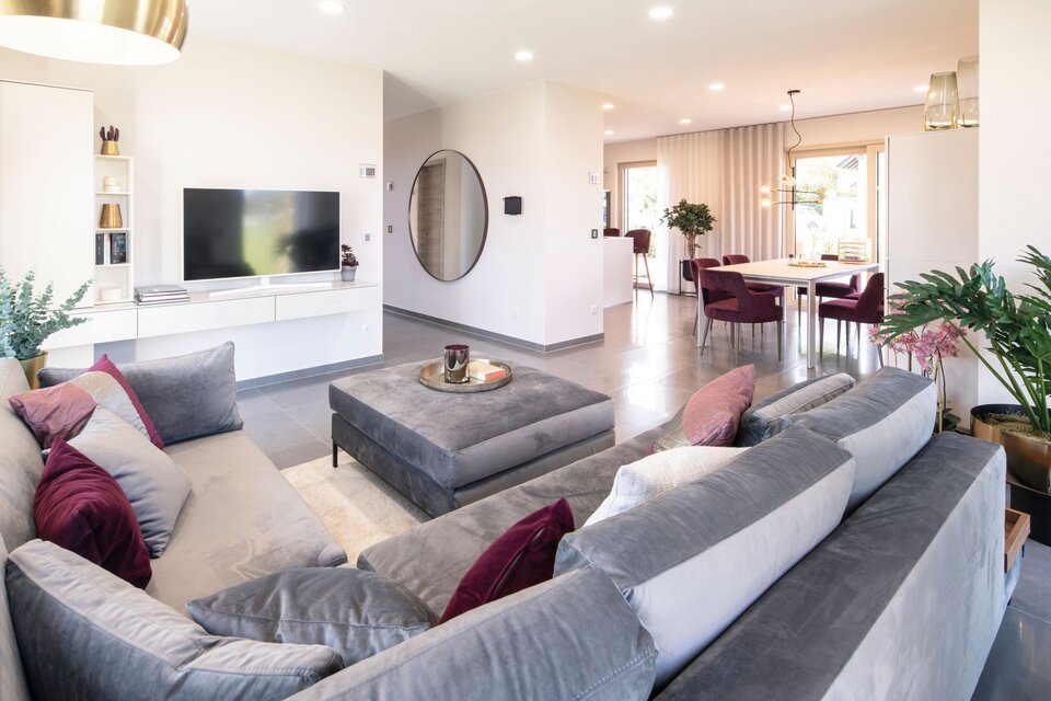 Helles Wohnzimmer im FingerHaus MEDLEY 300 B Musterhaus Frankenberg mit grauem Ecksofa, modernem TV-Bereich, großem Esstisch und stilvoller Dekoration.