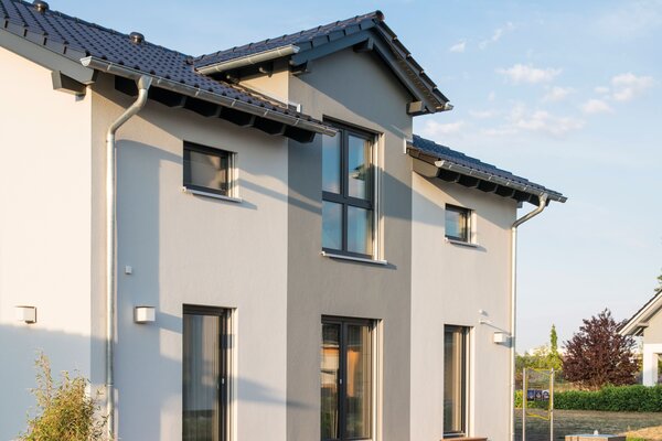 Seitenansicht des Musterhauses UNO 2.0 in Leipzig mit moderner Putzfassade, grauen Akzenten und großen Fensterflächen.