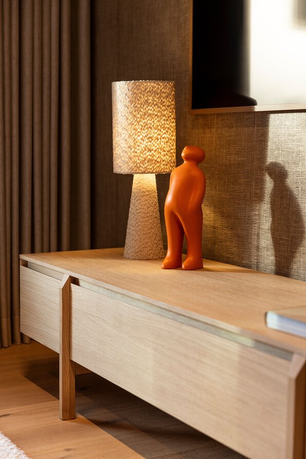 Detailaufnahme im FingerHaus Musterhaus NIVO in Frankenberg mit beleuchteter Tischlampe und orangefarbener Figur auf einem Holz-Sideboard.