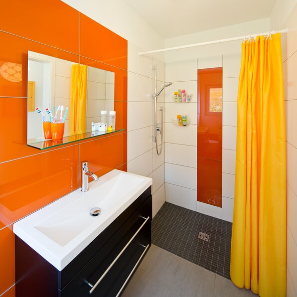 Modernes Badezimmer mit orangen Wandfliesen, gelbem Duschvorhang und weißem Waschtisch mit Spiegel.