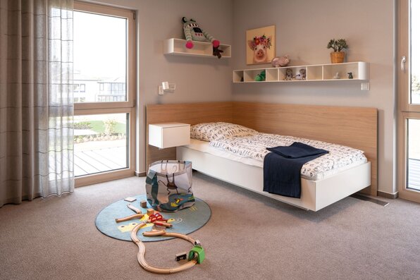 Helles Kinderzimmer im Musterhaus MEDLEY 300 B in Frankenberg mit Einzelbett, Spielteppich und kindgerechter Dekoration.