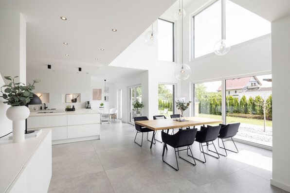Offener Wohnbereich in einem FingerHaus mit moderner weißer Küche, großem Esstisch, hohen Fenstern und lichtdurchflutetem Raum mit Blick in den Garten.
