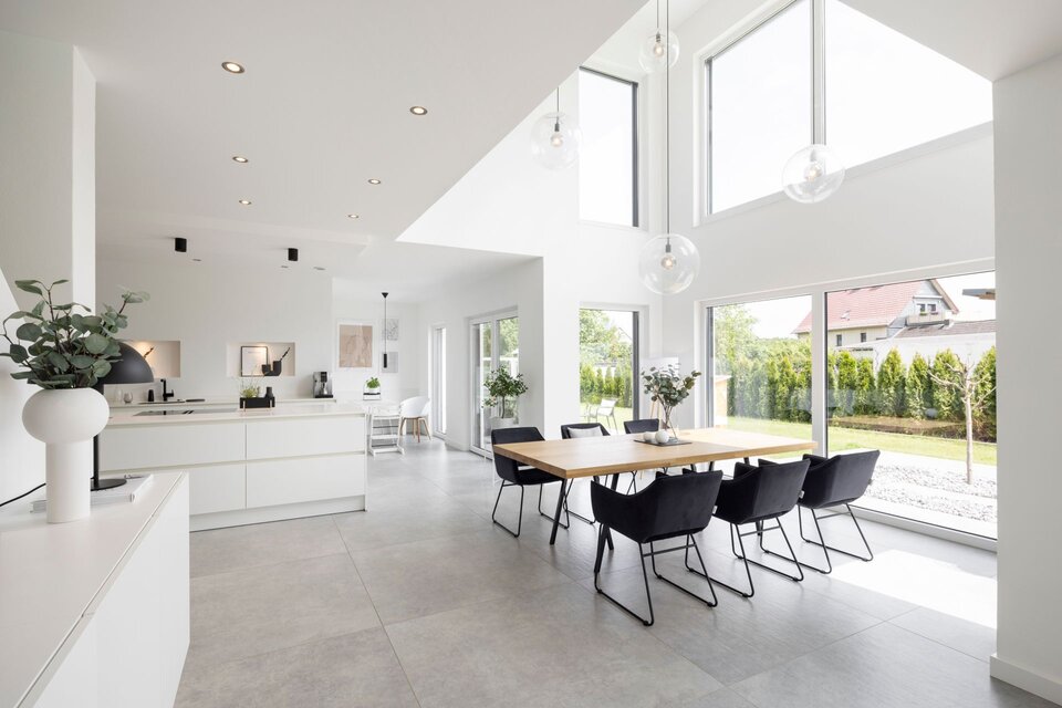 Offener Wohnbereich in einem FingerHaus mit moderner weißer Küche, großem Esstisch, hohen Fenstern und lichtdurchflutetem Raum mit Blick in den Garten.