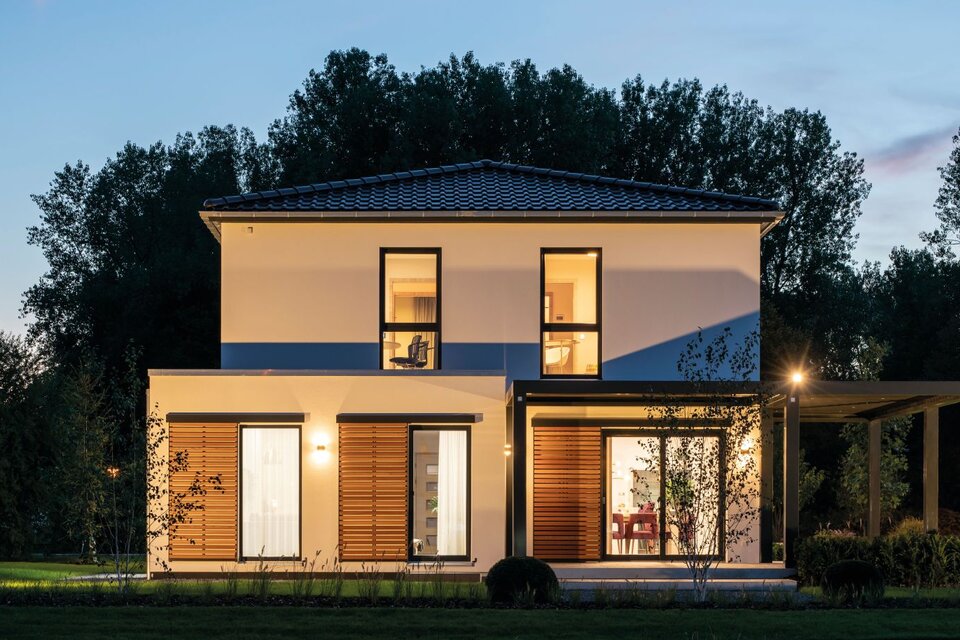 Beleuchtetes Musterhaus MEDLEY 300 B in Frankenberg bei Dämmerung mit klarer Architektur und Holzlamellen.