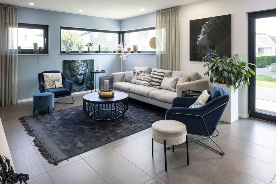 Wohnzimmer im Musterhaus VIO Köln mit grauem Sofa, blauen Sesseln, großformatiger Wandkunst und modernem Interieur.