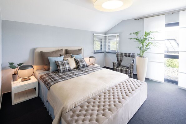Modern eingerichtetes Schlafzimmer im FingerHaus NEO 300 Musterhaus Hannover mit großem Doppelbett, gepolsterter Sitzbank und gemütlichem Sessel.