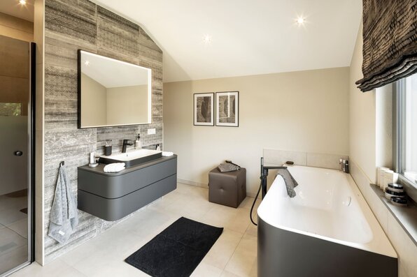 Helles Badezimmer im FingerHaus ARTIS 300 Musterhaus Würzburg mit moderner Badewanne, großem Spiegel und stilvoller Wandgestaltung.
