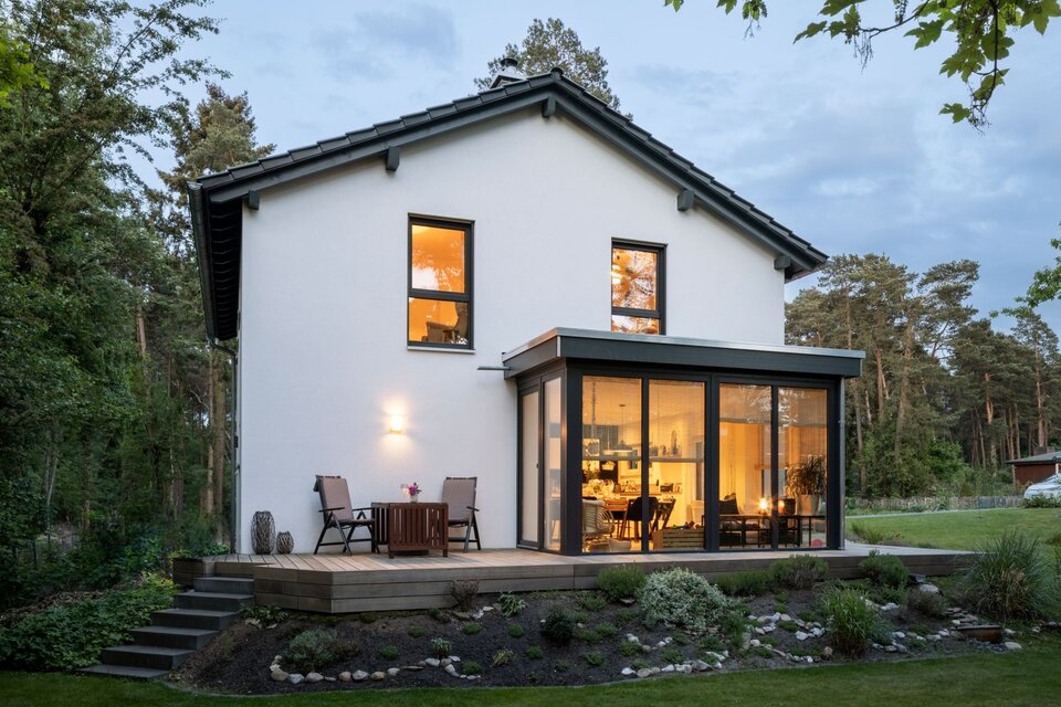 Frei geplantes FingerHaus mit Glasfassade und beleuchtetem Wohnbereich am Abend.