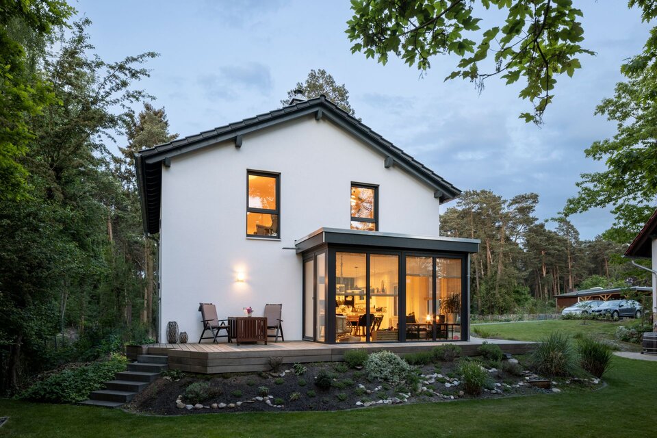 Frei geplantes FingerHaus mit Glasfassade und beleuchtetem Wohnbereich am Abend.