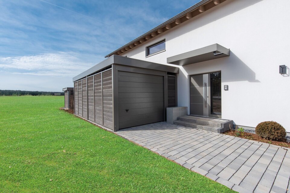 Eingangsbereich des Musterhauses TALO in Babenhausen mit moderner Haustür, überdachtem Eingang und angrenzender Garage in Holzoptik.