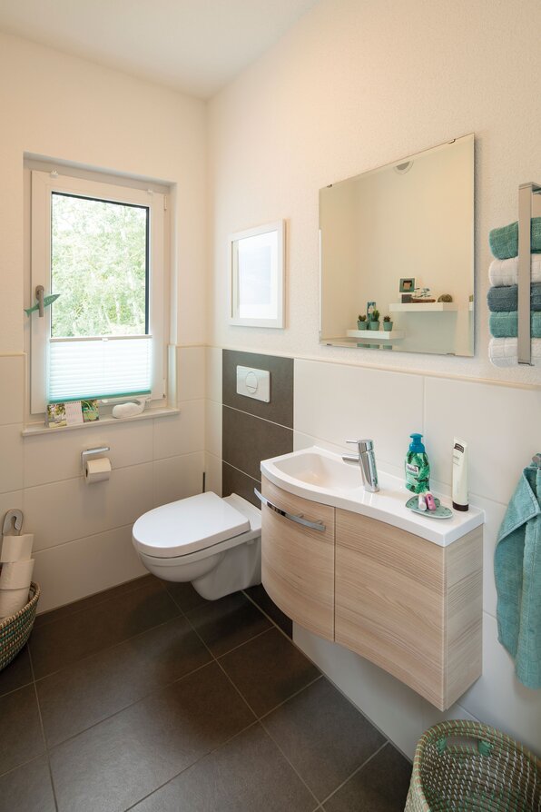 Modernes Gäste-WC in einem frei geplanten FingerHaus mit Hänge-WC, Waschbecken mit Holzfront, großem Spiegel und Fenster mit Tageslicht.