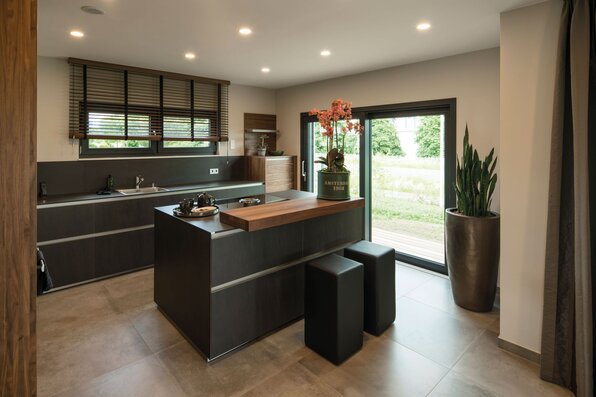 Moderne Küche im Musterhaus MAXIM in Gießen mit Kochinsel, eleganten schwarzen Fronten und großem Fenster mit Zugang zur Terrasse.