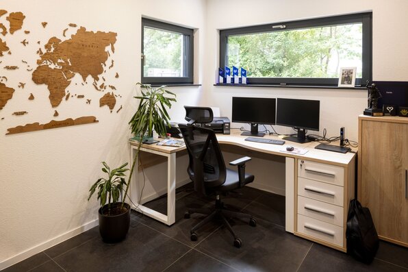 Helles Homeoffice mit Schreibtisch, zwei Monitoren, Wanddeko und großem Fenster.