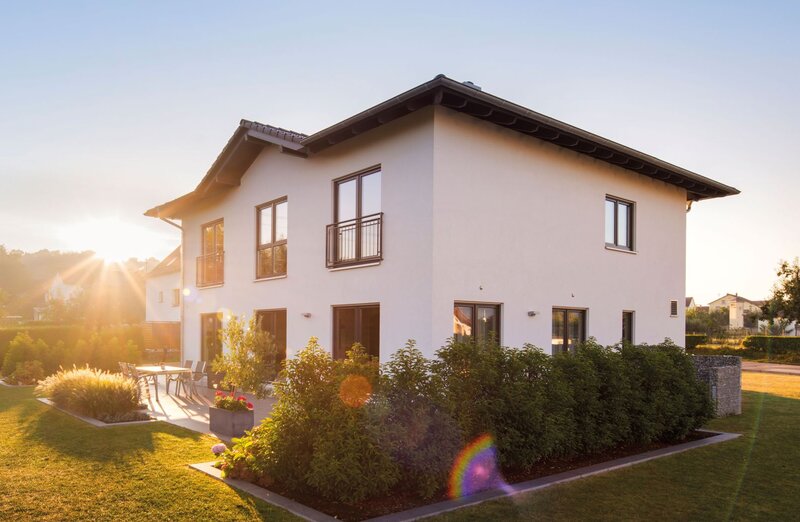 Modernes zweigeschossiges FingerHaus mit weißer Fassade, dunklem Satteldach, Terrasse und gepflegtem Garten, aufgenommen bei Sonnenuntergang.