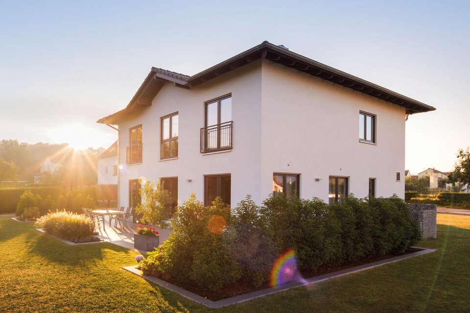 Modernes zweigeschossiges FingerHaus mit weißer Fassade, dunklem Satteldach, Terrasse und gepflegtem Garten, aufgenommen bei Sonnenuntergang.
