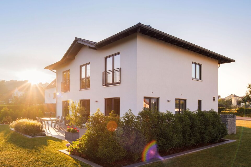 Modernes zweigeschossiges FingerHaus mit weißer Fassade, dunklem Satteldach, Terrasse und gepflegtem Garten, aufgenommen bei Sonnenuntergang.