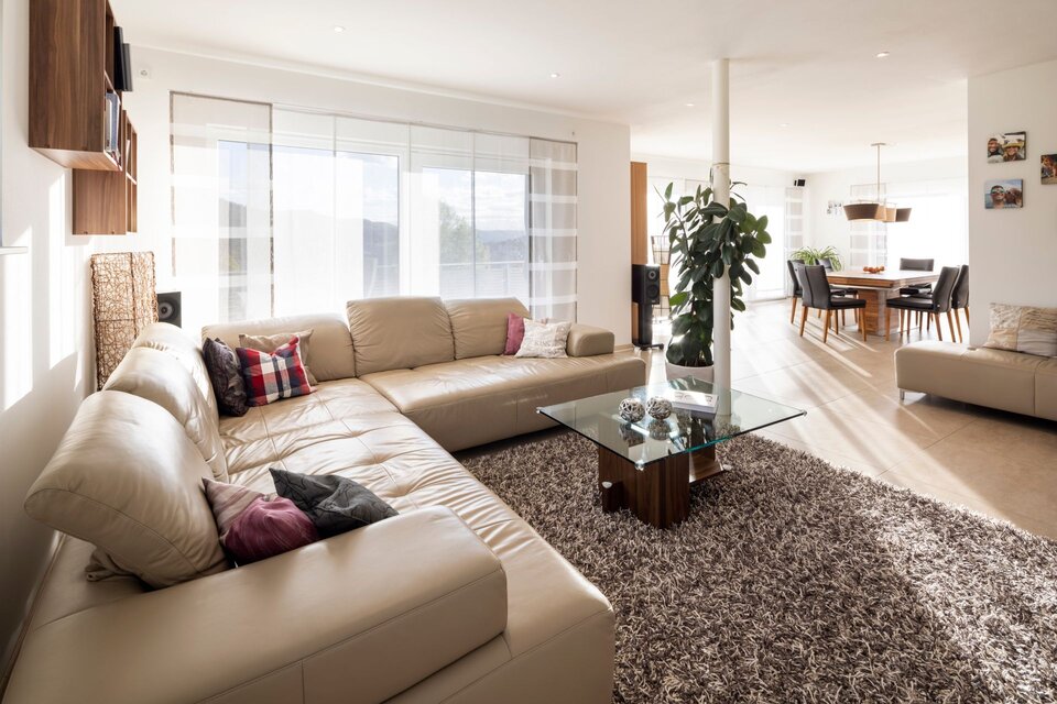 Helles Wohnzimmer mit offener Verbindung zum Essbereich, großer Ledercouch und modernem Glastisch im frei geplanten FingerHaus.