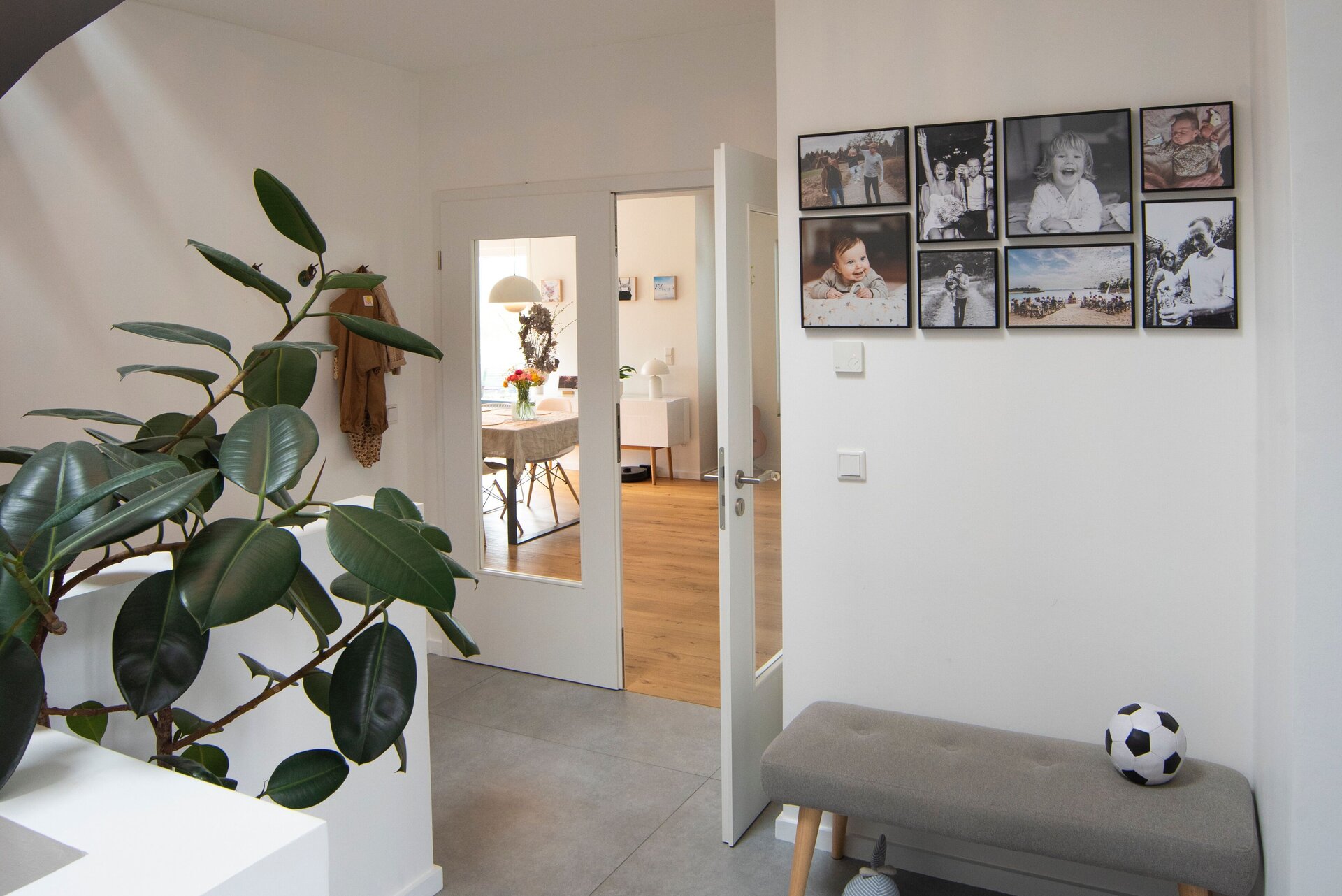 Heller Eingangsbereich in einem frei geplanten FingerHaus mit modernen Fliesen, Sitzbank, Kinderfahrzeug und Blick in den Wohnbereich.