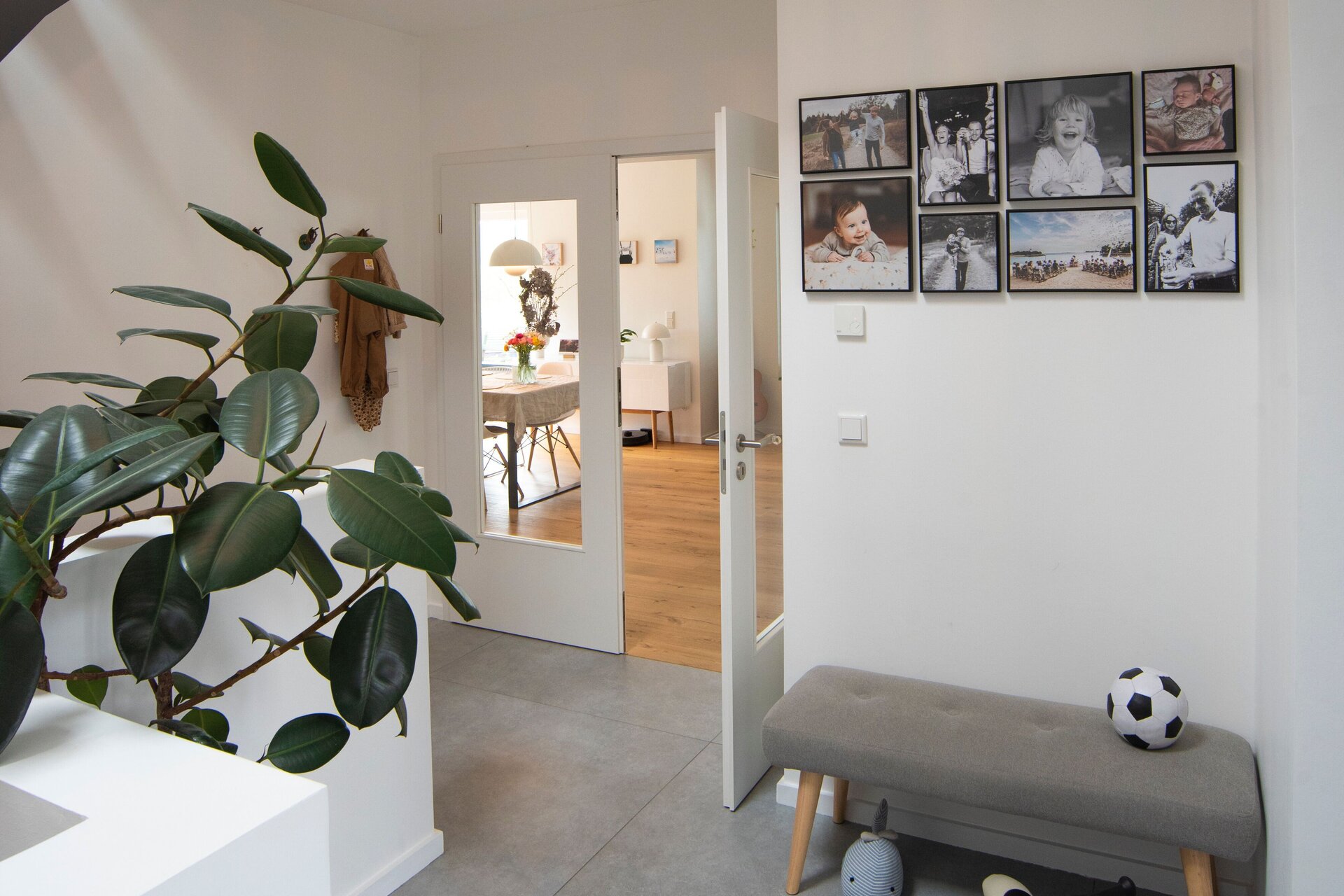 Heller Eingangsbereich in einem frei geplanten FingerHaus mit modernen Fliesen, Sitzbank, Kinderfahrzeug und Blick in den Wohnbereich.