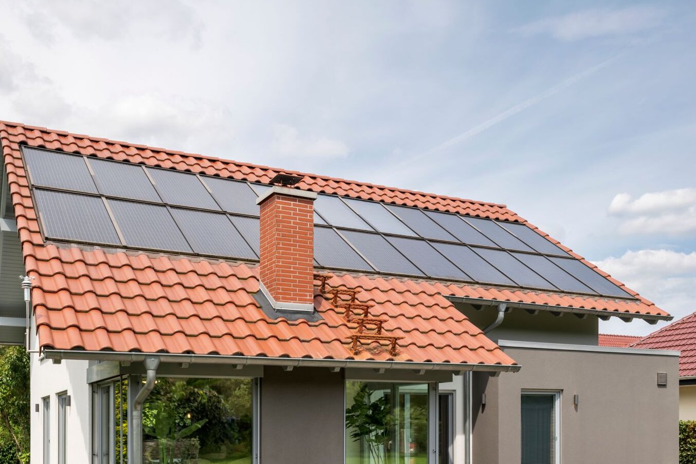 Außenansicht des frei geplanten FingerHaus Musterhauses in Marburg mit rotem Satteldach, Photovoltaikanlage und großem Wintergarten.