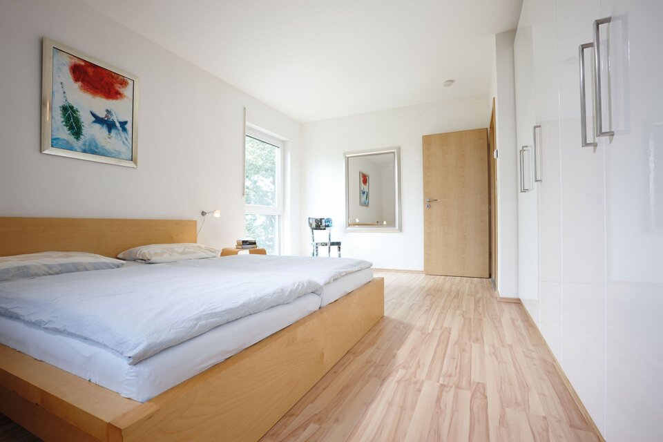 Helles Schlafzimmer mit Holzboden, großem Bett und weißen Einbauschränken.