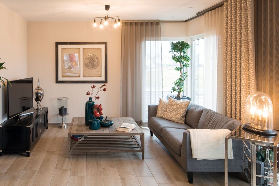 Wohnzimmer im FingerHaus MEDLEY 300 B Musterhaus Berlin/Werder mit grauem Sofa, modernem Couchtisch und stilvoller Dekoration.