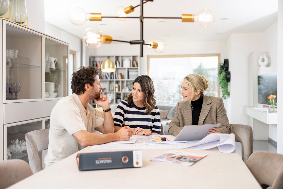 Architektengespräch bei FingerHaus – ein Paar sitzt mit einer Architektin am Esstisch und bespricht Baupläne in moderner, heller Wohnatmosphäre.