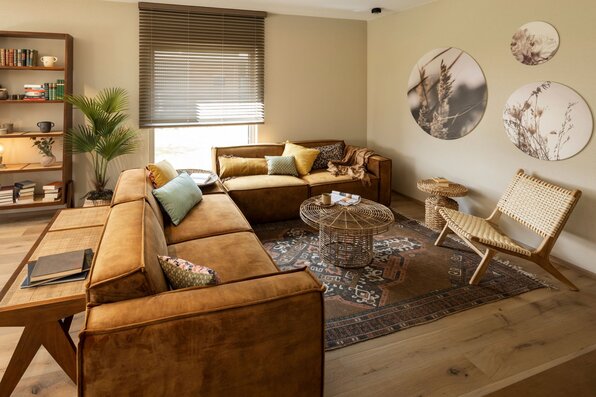 Wohnzimmer im FingerHaus ARTIS 400 Musterhaus Schwarzwald mit großem Ecksofa in Lederoptik, Rattanstühlen, Couchtisch und dekorativem Teppich.