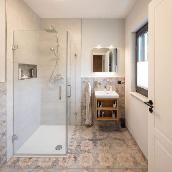 Frei geplantes FingerHaus mit modernem Badezimmer, Glasdusche und stilvollen Fliesen.