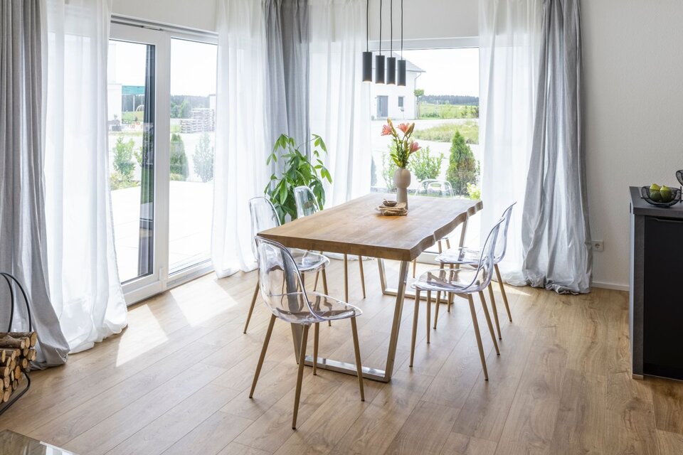 Offener Essbereich mit Blick zur Küche; bodentiefe Fenster, natürliche Materialien und harmonische Raumgestaltung.