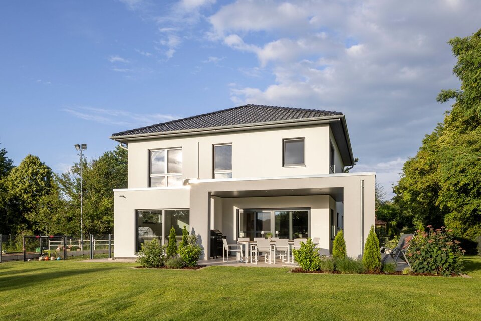 Moderne Stadtvilla von FingerHaus mit weißer Fassade, überdachter Terrasse und gepflegtem Garten im Abendlicht.