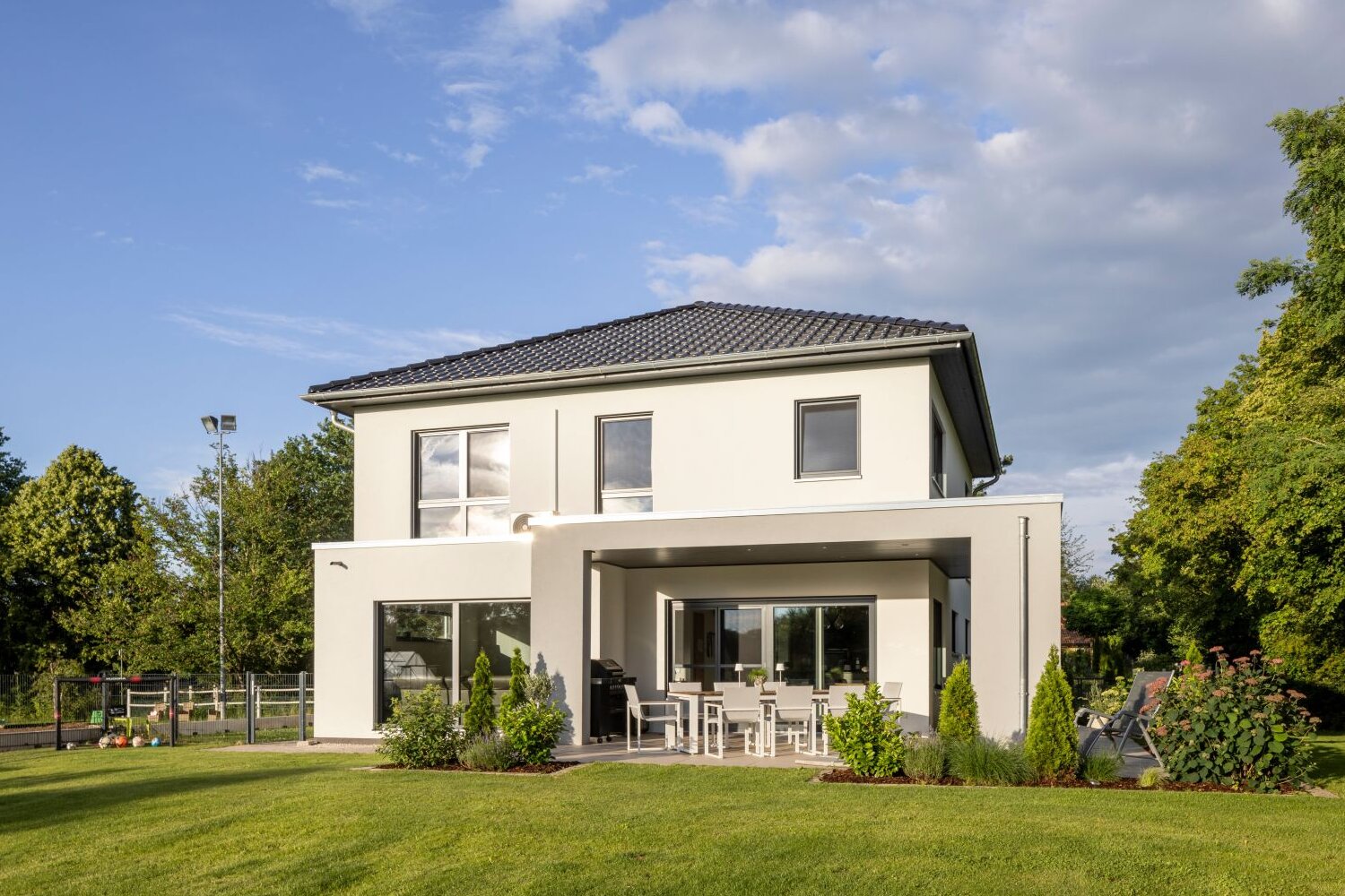 Moderne Stadtvilla von FingerHaus mit weißer Fassade, überdachter Terrasse und gepflegtem Garten im Abendlicht.