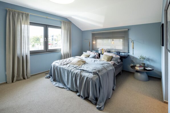 Modernes Schlafzimmer im FingerHaus ARTIS 300 Musterhaus Würzburg mit blauen Wänden, Doppelbett und großen Fenstern.