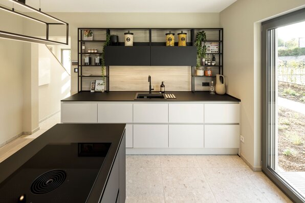 Moderne Küche im FingerHaus ARTIS 300 Musterhaus Würzburg mit Kochinsel, schwarzen Oberflächen und großen Glasfronten.