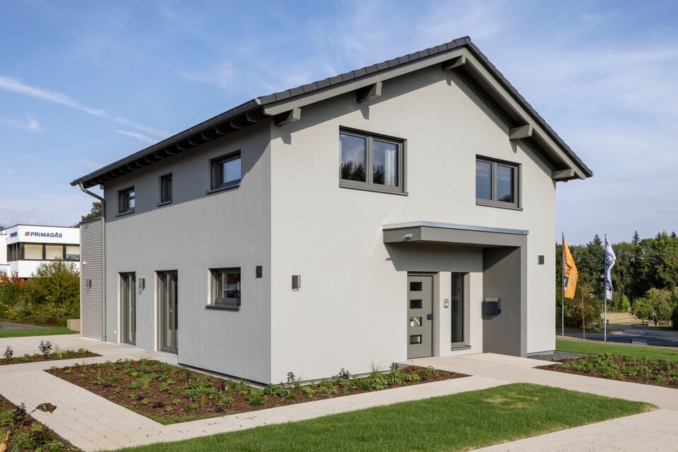 Außenansicht des FingerHaus ARTIS 300 Musterhauses Würzburg mit grauer Putzfassade, Satteldach und modern gestaltetem Vorgarten.