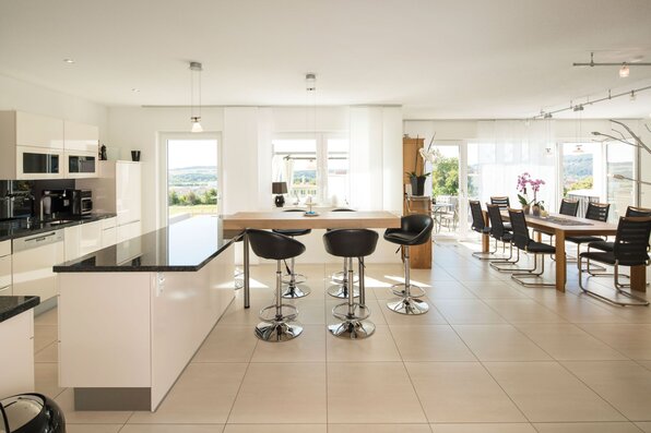 Offene Wohnküche in einem frei geplanten FingerHaus mit moderner Kochinsel, Barhockern und großem Essbereich mit Panoramablick.