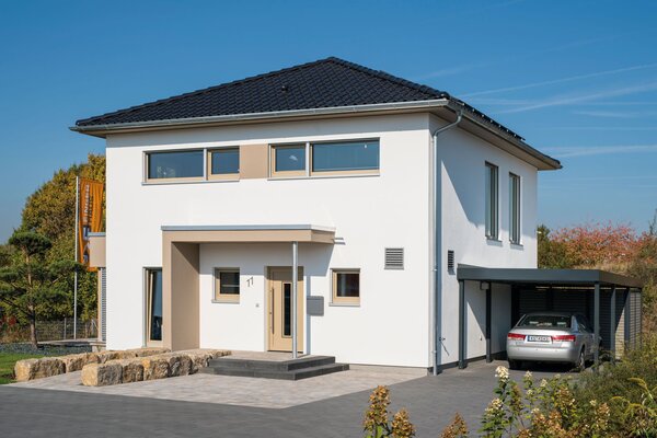 Musterhaus MEDLEY 300 B in Kassel mit Walmdach, modernem Eingangsbereich und angrenzendem Carport mit geparktem Auto.