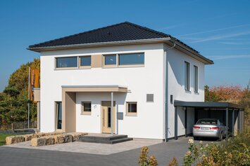 Musterhaus MEDLEY 300 B in Kassel mit Walmdach, modernem Eingangsbereich und angrenzendem Carport mit geparktem Auto.
