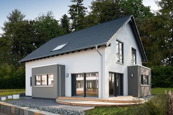Modernes Musterhaus mit Satteldach und zweifarbiger Putzfassade in Weiß und Grau. Vor dem Haus befindet sich eine Holzterrasse, eingerahmt von Zierkies und einer niedrigen Natursteinmauer.