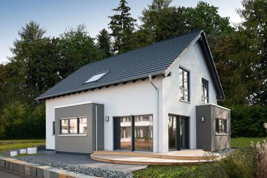 Modernes Musterhaus mit Satteldach und zweifarbiger Putzfassade in Weiß und Grau. Vor dem Haus befindet sich eine Holzterrasse, eingerahmt von Zierkies und einer niedrigen Natursteinmauer.